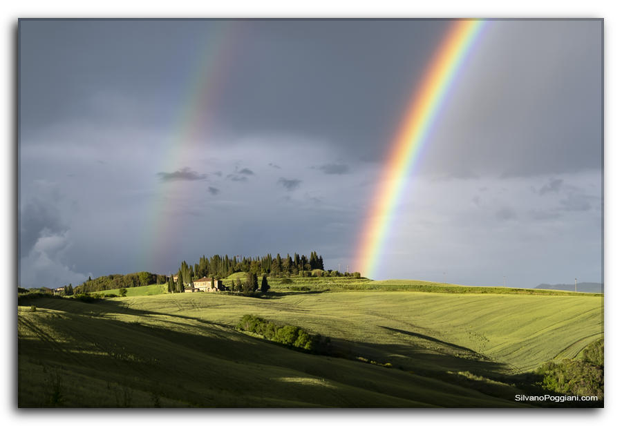 Podere toscano nella verde collina, arcobaleno vivido nel cielo plumbeo.